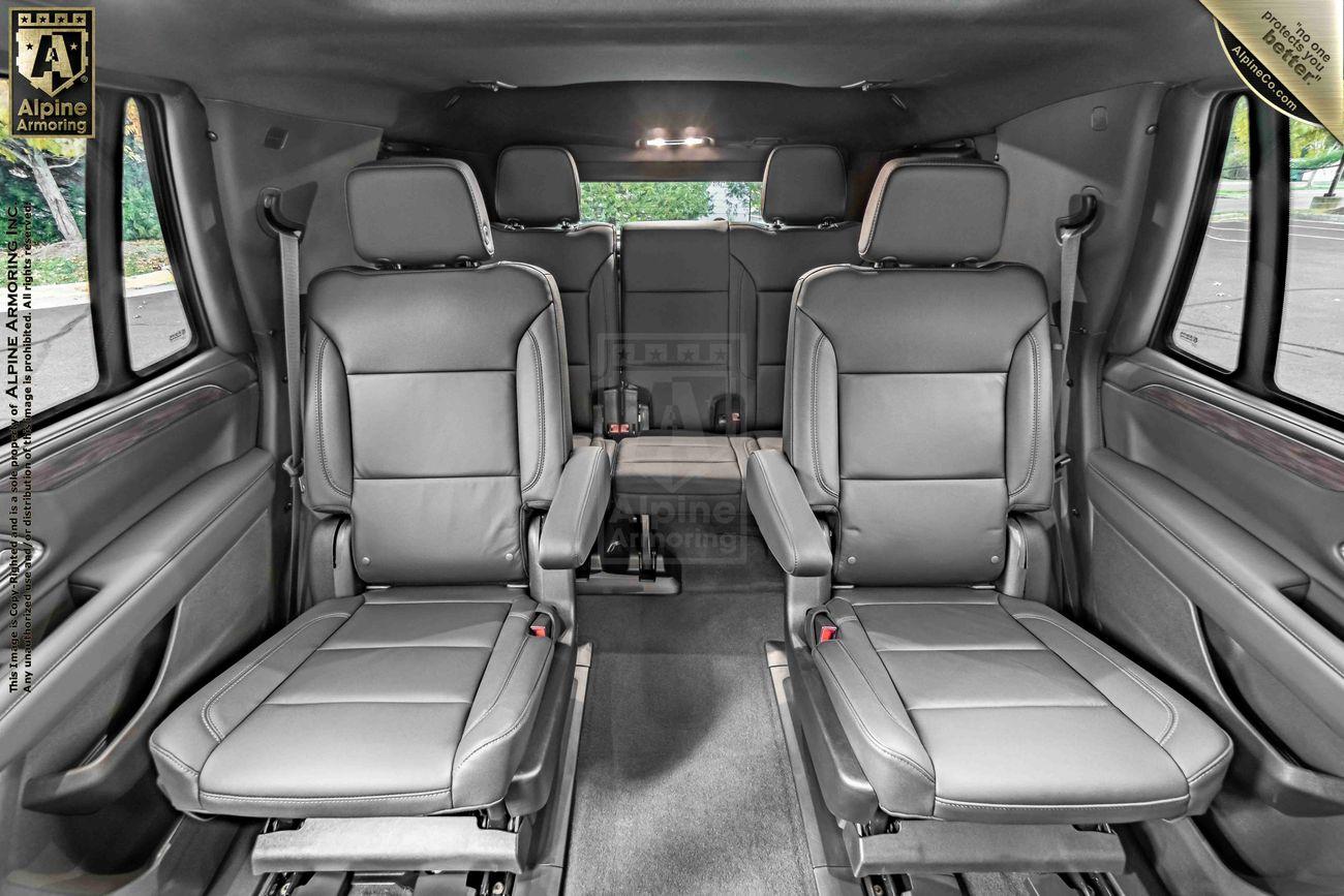 Interior of a bulletproof black Chevrolet Tahoe SUV with two rows of gray leather captain's chairs and a third row in the back, designed with ample legroom and modern features.