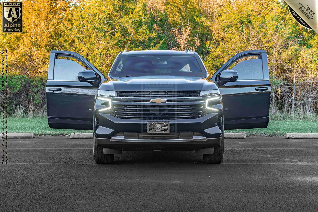 An armored black Chevrolet Tahoe SUV is parked with its front doors open. The vehicle is positioned on a paved surface with trees in the background and a "Platinum Certified" badge in the top right corner.