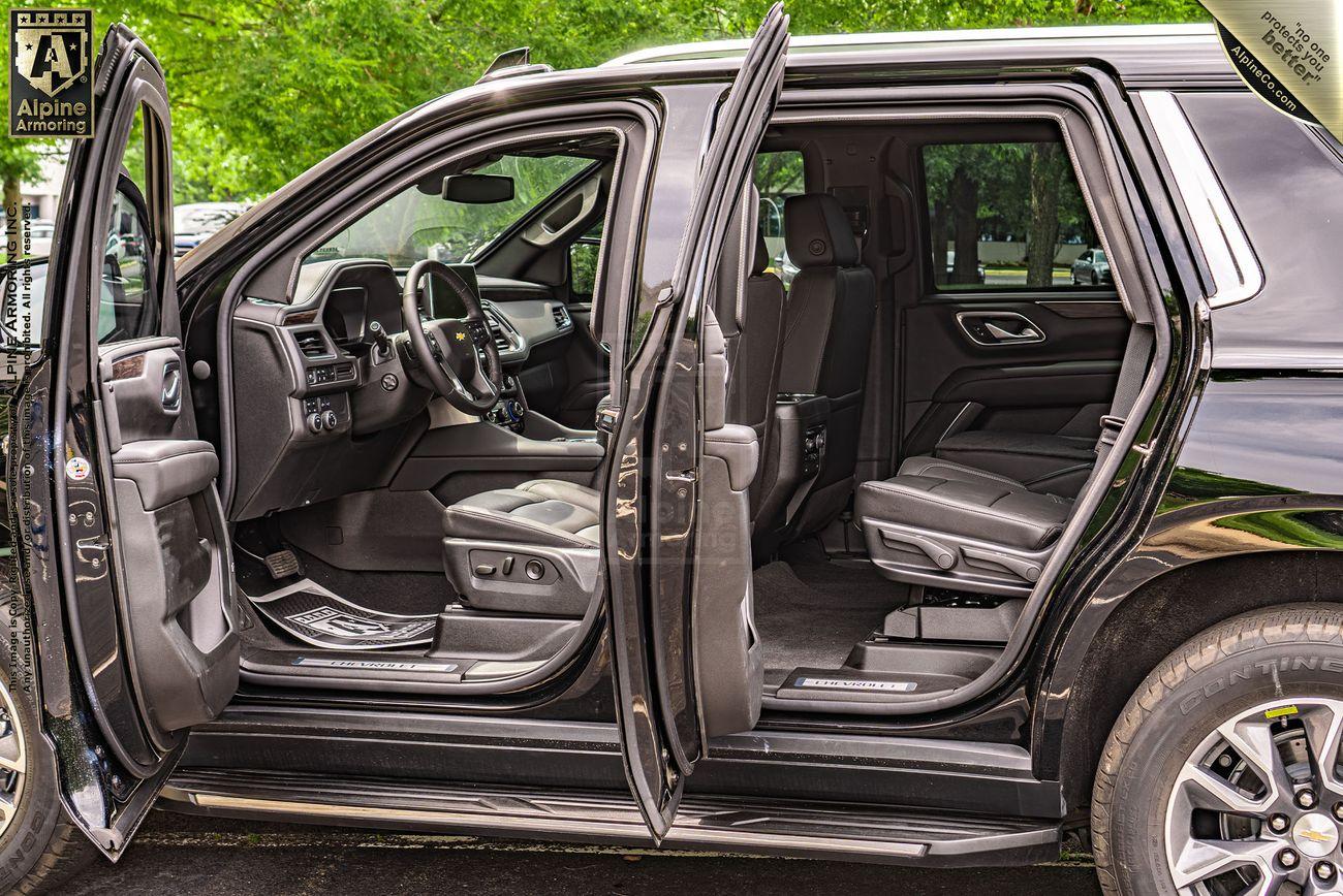 A black Chevrolet Tahoe SUV with its driver and rear passenger doors open, showing the interior seating and dashboard. Forested area is visible in the background.