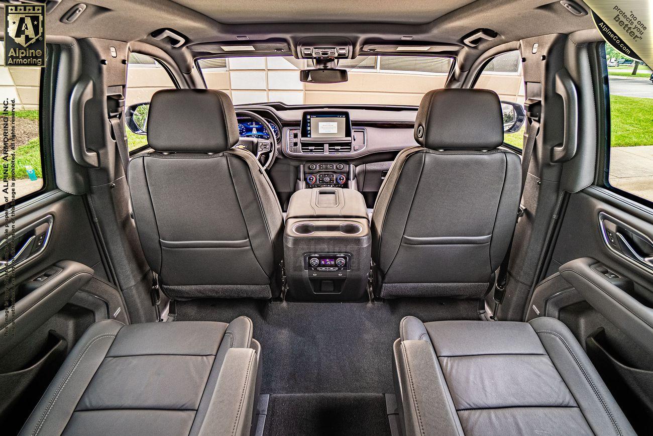 Interior of an armored Chevrolet Tahoe SUV showing three rows of black leather seats, a console in the middle row, and a dashboard with digital displays at the front.