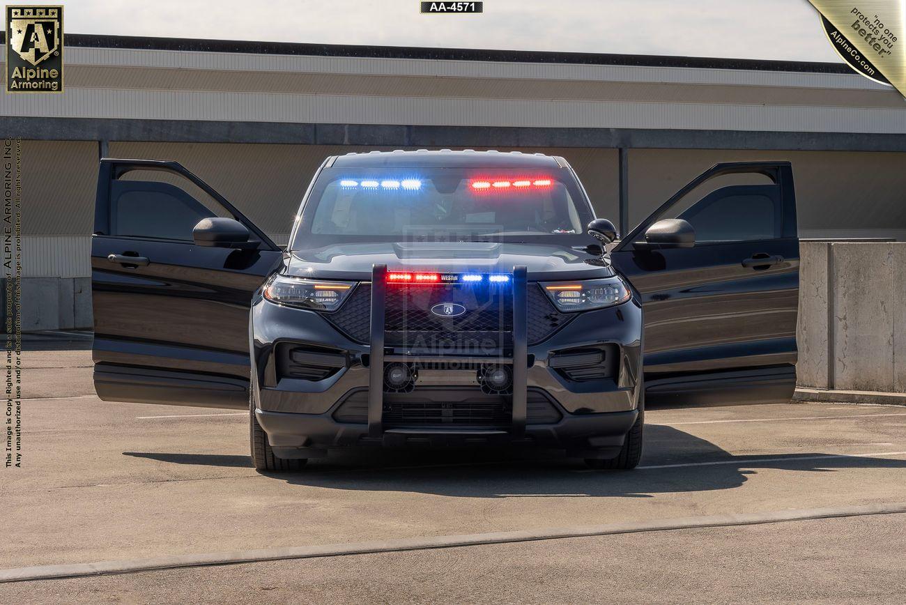 A black police Ford Explorer PPV with its blue and red emergency lights turned on, positioned in front of a building with both front doors open.