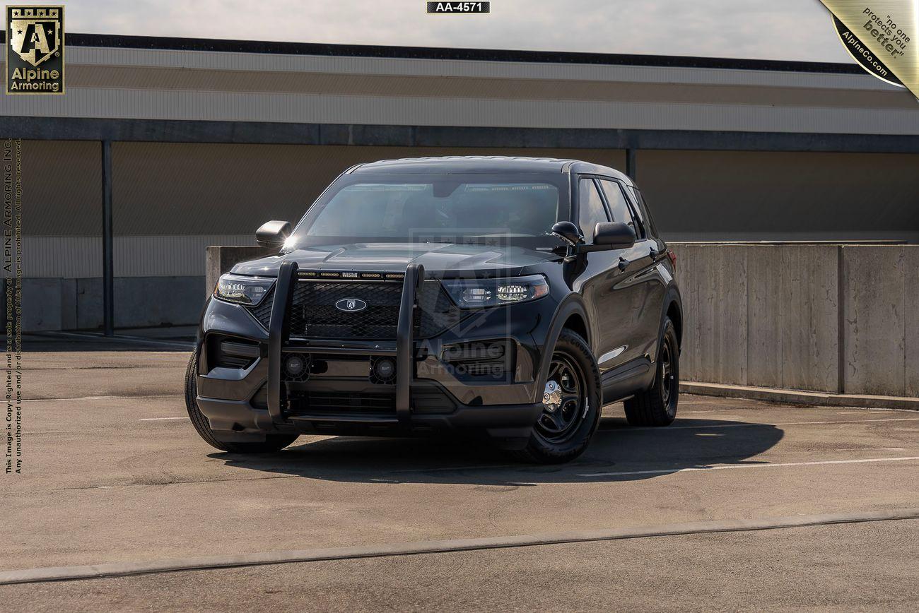 A black police Ford Explorer PPV SUV equipped with a push bumper is parked in an empty lot with a building in the background.