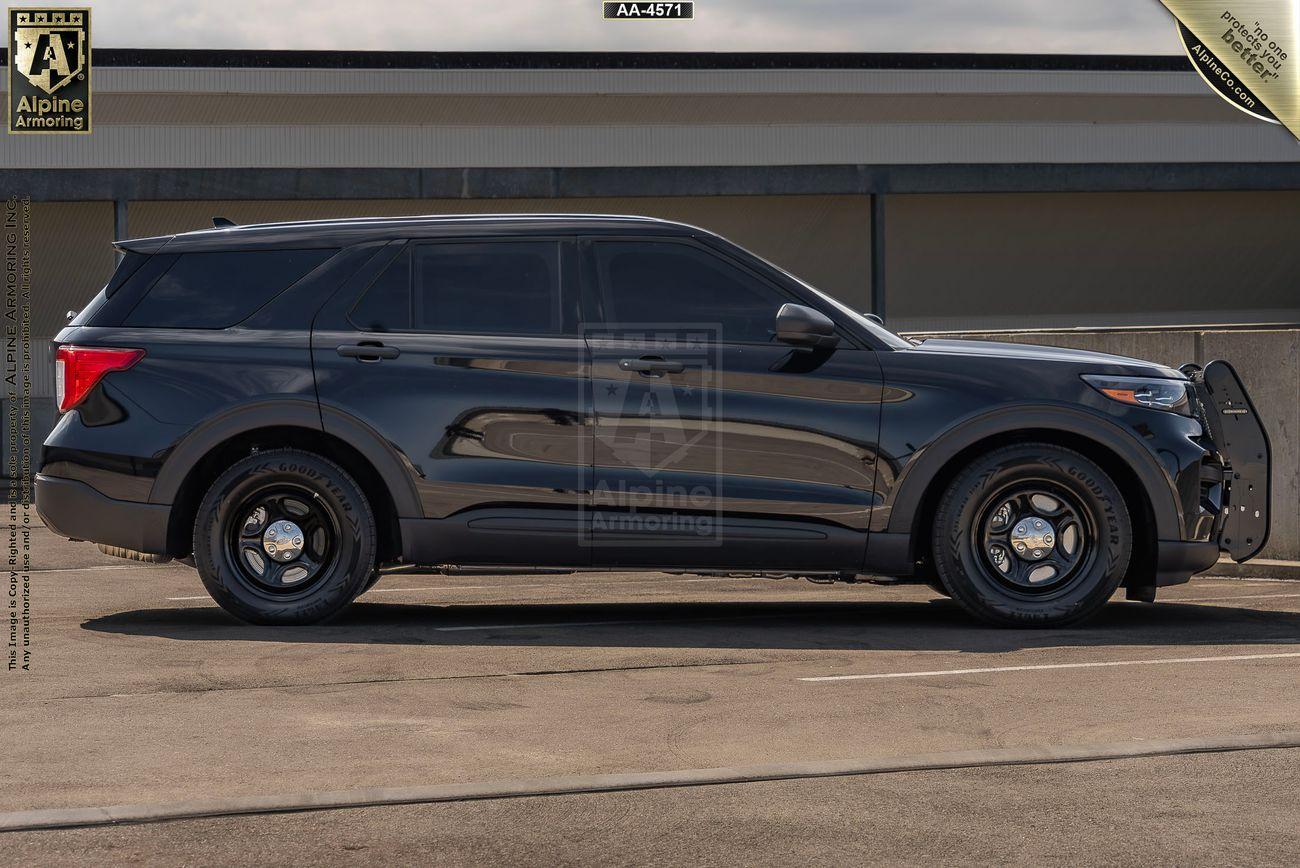 A black bulletproof Ford Explorer SUV with law enforcement markings is parked outside a building. The vehicle has tinted windows, black rims, and a push bumper at the front.