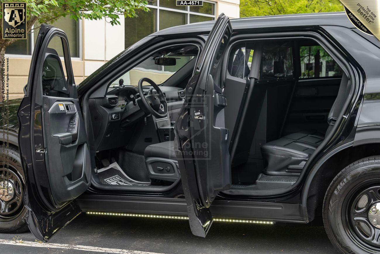 Image of a black Ford Explorer PPV with both the front and rear passenger doors open, revealing the interior seats and dashboard. The vehicle is parked outside a building, with a partially visible license plate overhead.