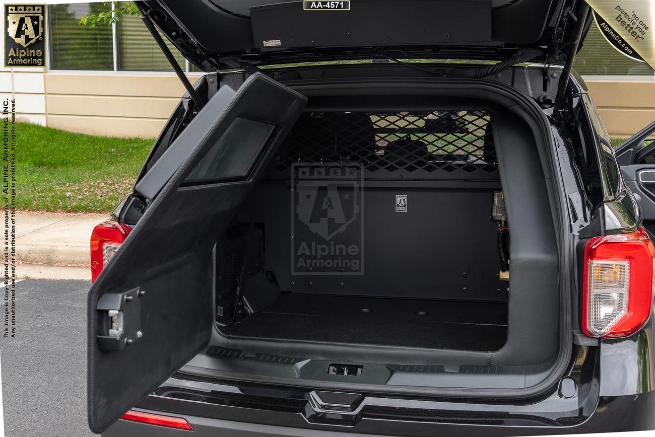 The open trunk of an armored  Ford Explorer PPV SUV shows a secure interior compartment with a mesh divider. Logos and branding of Alpine Armoring are visible inside and on the open trunk door.