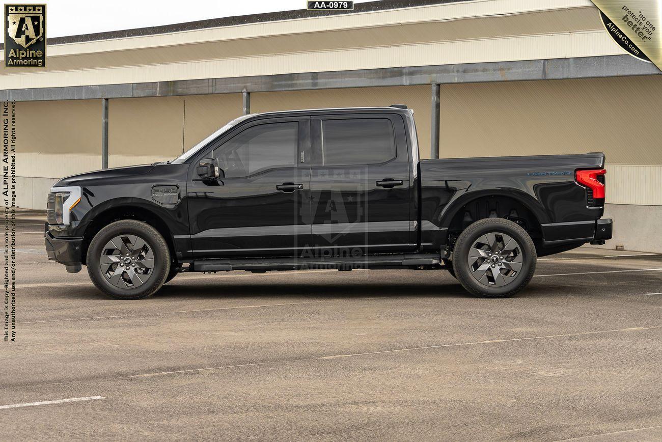 Black armored Ford Lightning truck parked in an empty parking lot in front of a beige building.