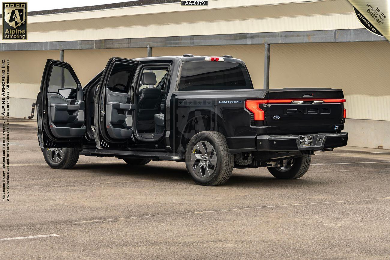 Black armored Ford Lightning truck shown from the rear with both driver side doors open.  The setting is in a parking lot.