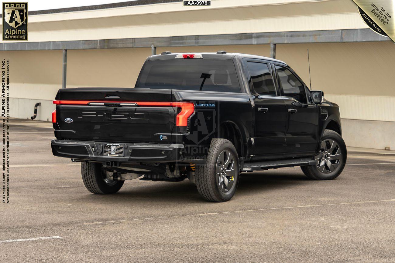 Rear-right view of a black armored Ford Lightning truck. Setting is in a parking lot.