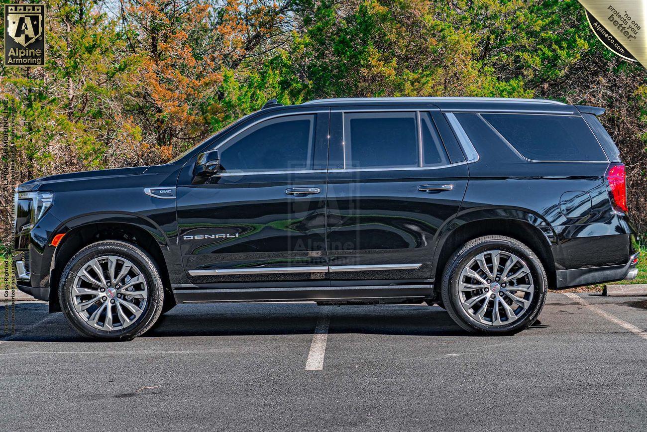 A side view of a black armored GMC Yukon Denali XL parked on a road. The SUV features tinted windows, chrome accents, large alloy wheels, and is captured from the driver's side, showing the full length from the front to the rear. 