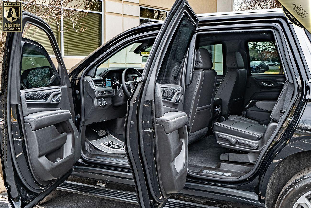 A black armored GMC Yukon Denali XL parked with its front and rear passenger-side doors open. The interior features black leather seats and modern dashboard controls. The setup highlights spaciousness and luxury. 