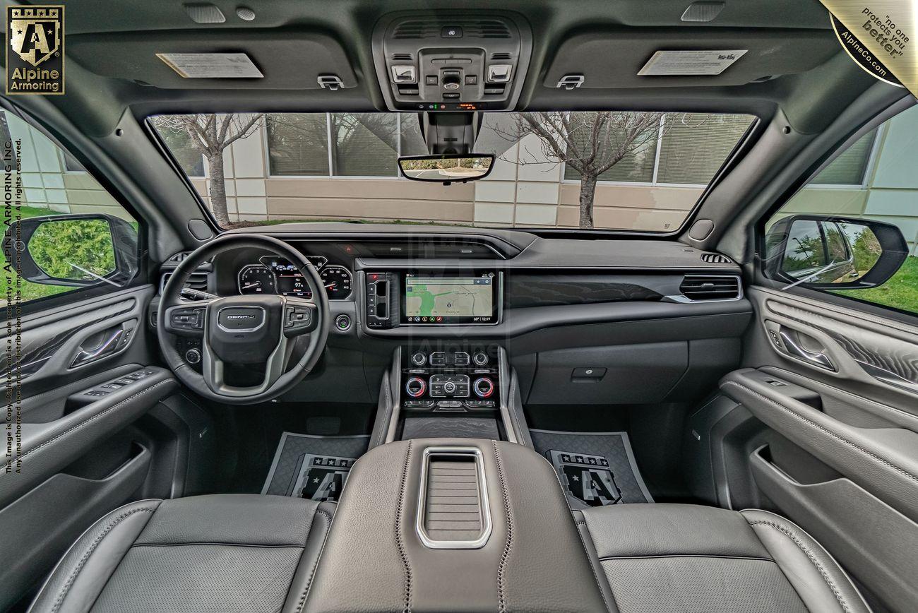 Interior view of an armored GMC Yukon Denali SUV highlighting the dashboard, steering wheel, touchscreen display, and front seats with a sunroof overhead.