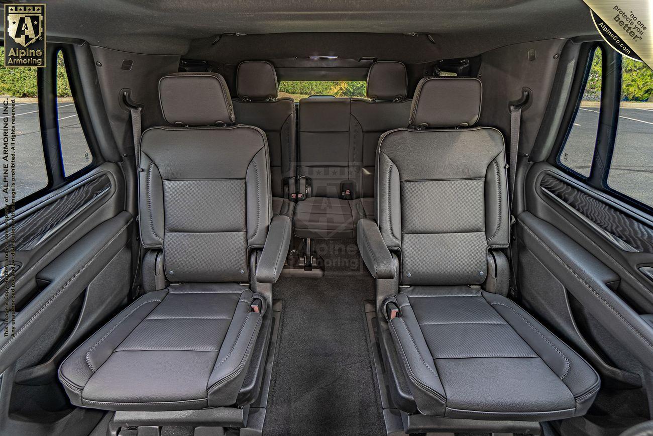 Interior of an armored GMC Yukon Denali showcasing two middle-row captain seats and a rear bench seat, all upholstered in gray leather. The seats are spacious with ample legroom on a clean, carpeted floor.