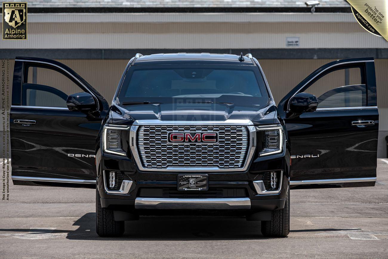 A black GMC Yukon Denali XL SUV is displayed with its front doors open in a parking lot, showcasing its front grille and headlight design. The vehicle is positioned in front of a garage door.