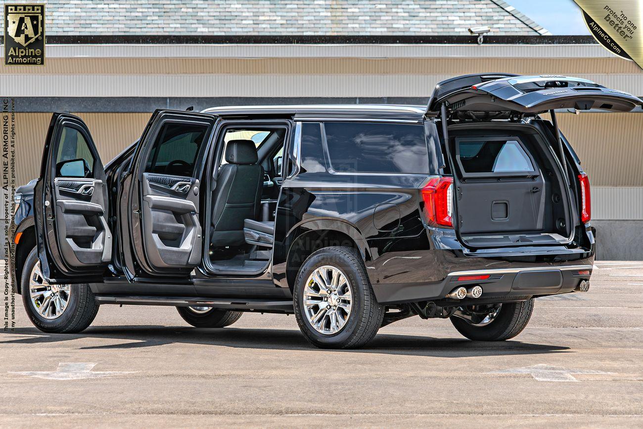 Driver side view of a black GMC Yukon Denali XL with all passenger doors and the rear hatch open, showing the interior and cargo space. The vehicle is parked on a concrete surface in front of a building.