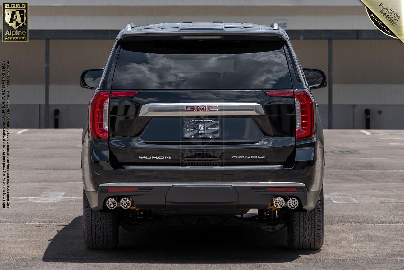 Rear view of a parked black armored GMC Yukon Denali XL .  The setting is a parking lot.