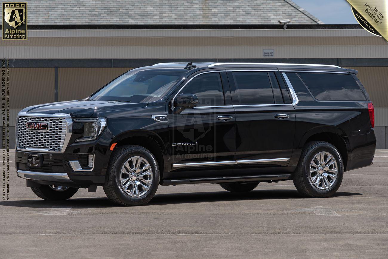 A black armored GMC Yukon Denali XL is parked on a paved surface in front of a building with a gray roof.