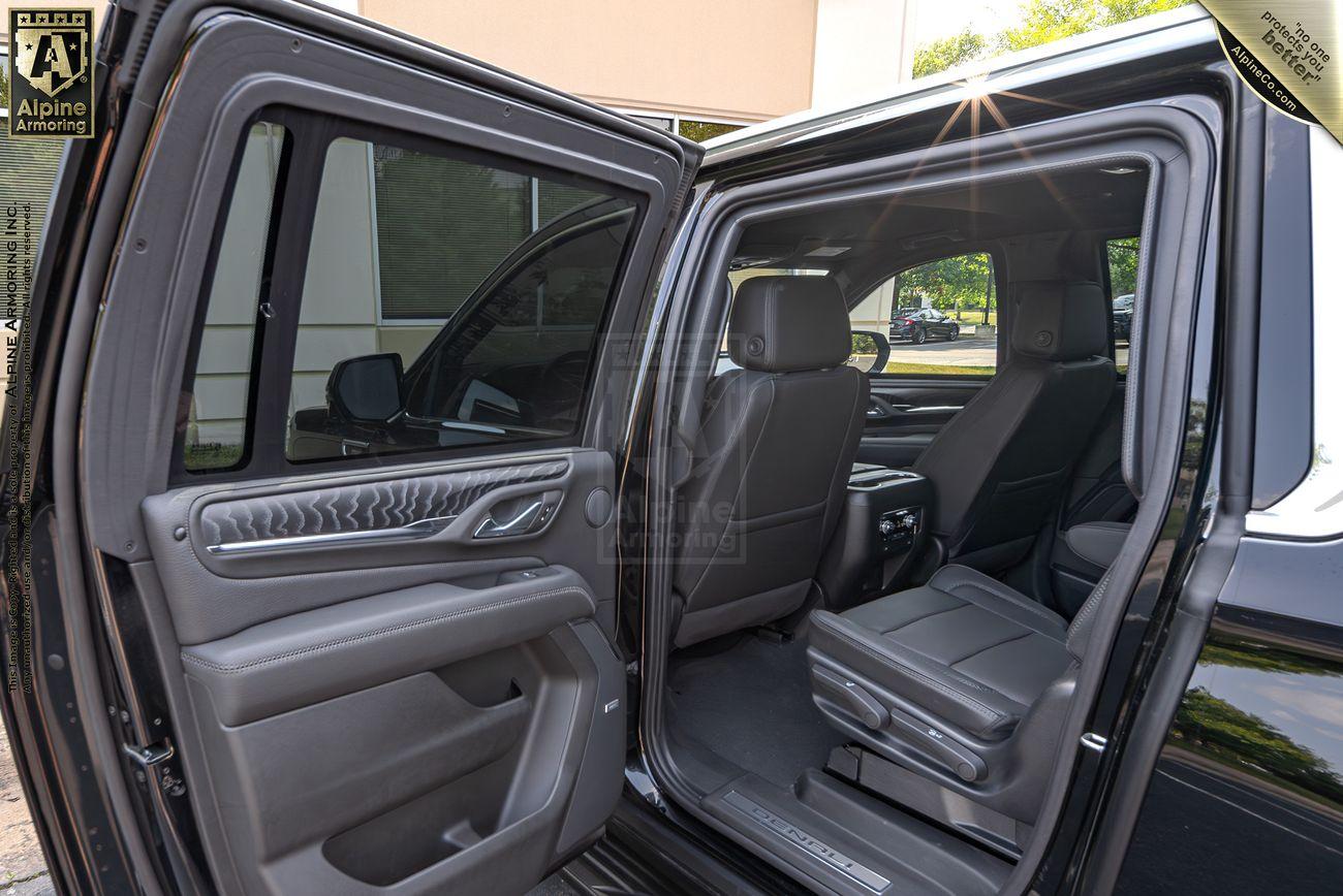 The open rear door of a black armored GMC Yukon Denali XL, providing a view of the spacious interior, including two black leather seats and the interior of one front seat and door.