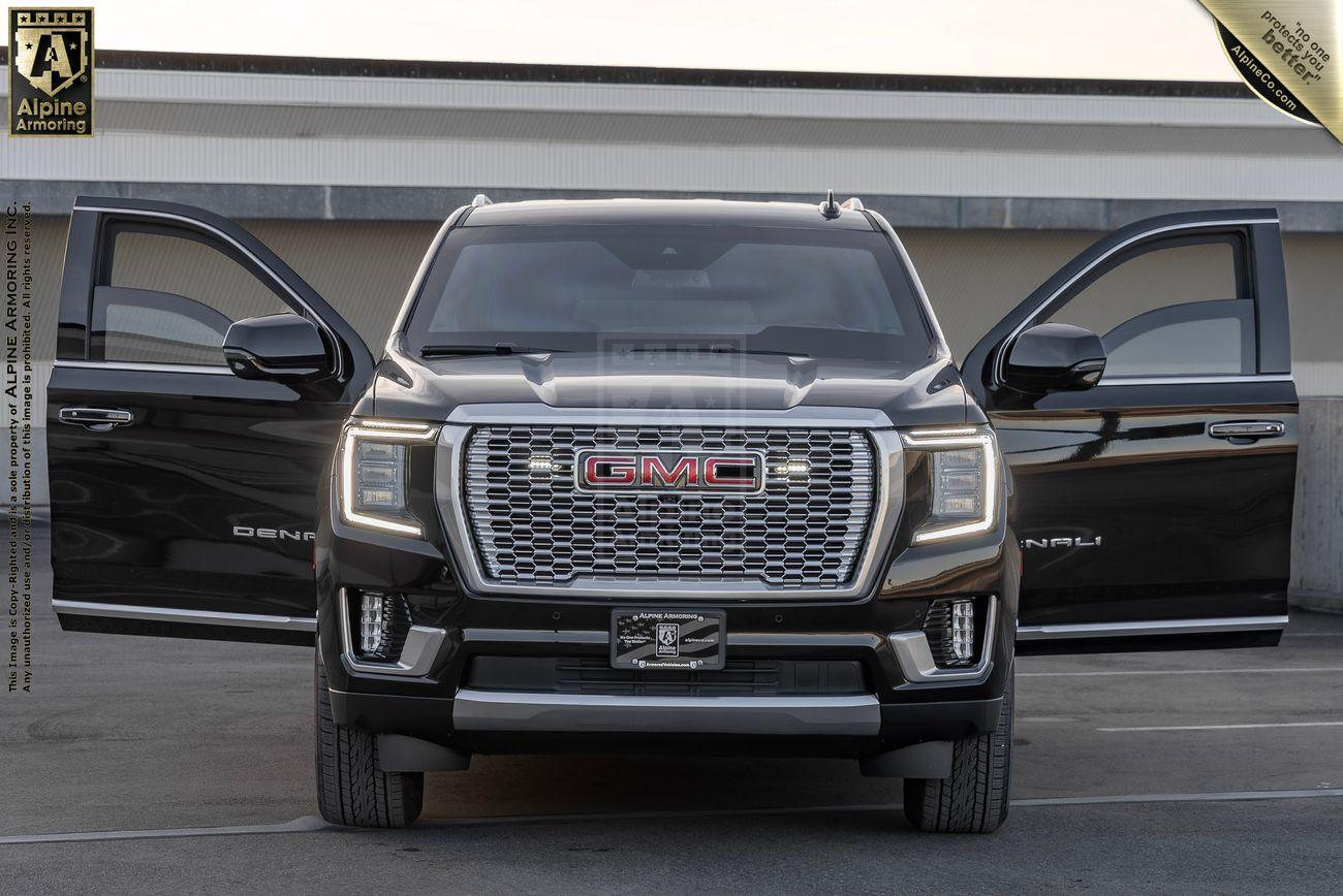 Front view of an armored GMC Yukon Denali XL truck with both front doors open, parked in an outdoor setting.