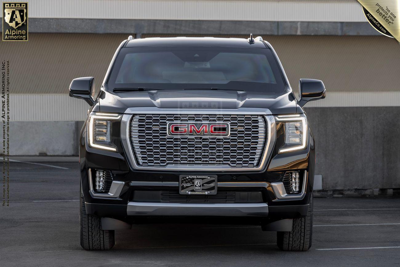 Front view of a black armored GMC Yukon Denali XL parked in a concrete lot. The vehicle has a large grille with the GMC logo in the center, LED headlights, and chrome accents.