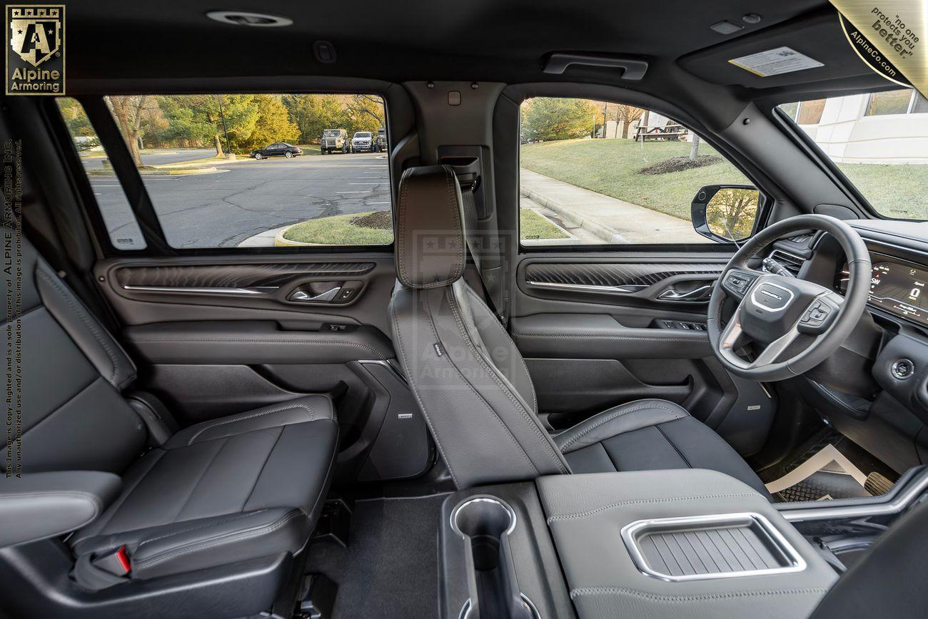 Interior of an armored GMC Yukon Denali XL SUV , featuring black leather seats, a central console with cup holders, various controls, and a digital display on the dashboard. The driver and passenger doors are open.