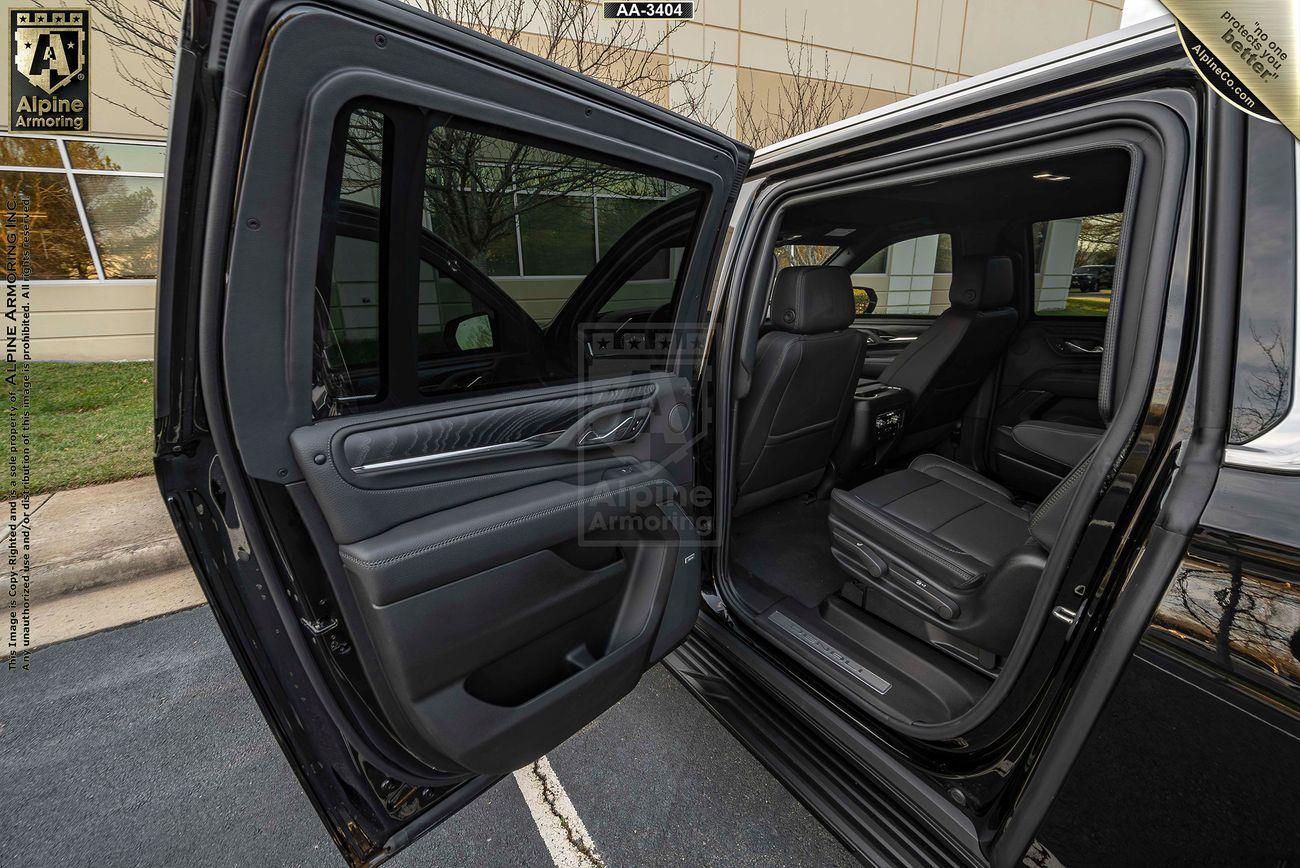 The open rear passenger door of a black armored GMC Yukon Denali XL SUV, displaying the spacious black interior seats and upholstery. The vehicle is parked outside, with a building visible in the background.