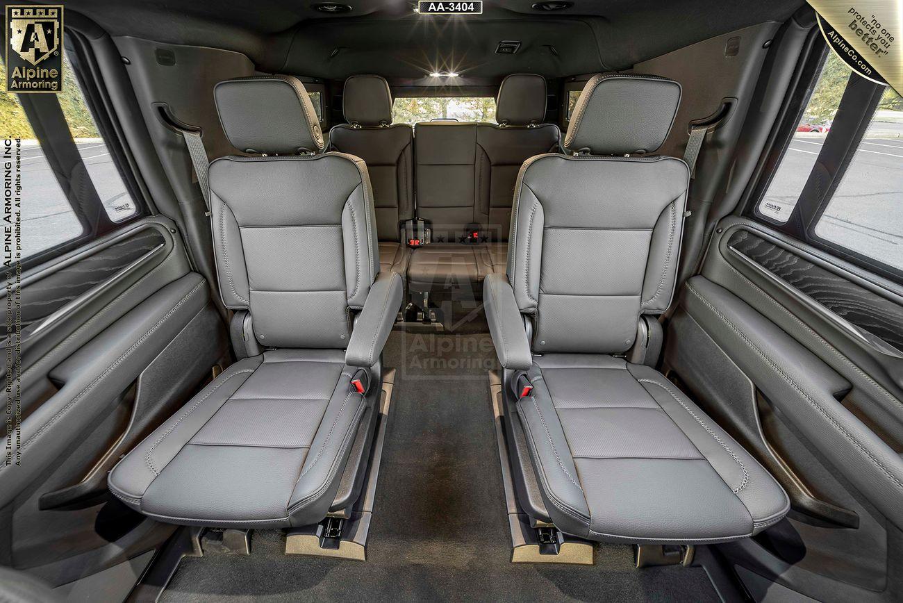 Interior of a GMC armored GMC Yukon Denali XL showing four leather seats, two in the middle row facing forward, and two in the rear. The seats feature armrests, and the car has large windows on the sides.