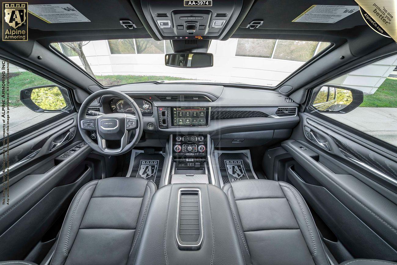 Interior view of a armored GMC Yukon Denali XL SUV featuring a sleek dashboard, a large touchscreen display, leather seats, and various control buttons. "Alpine Amazing" branding is visible.