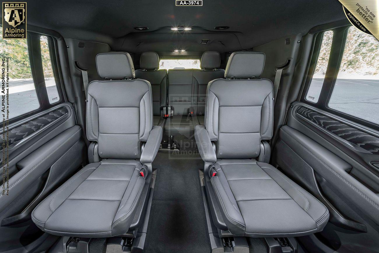 Spacious interior of a luxury armored GMC Yukon Denali XL with gray leather seating, featuring two captain chairs in the center row and a bench seat in the back, all facing forward.