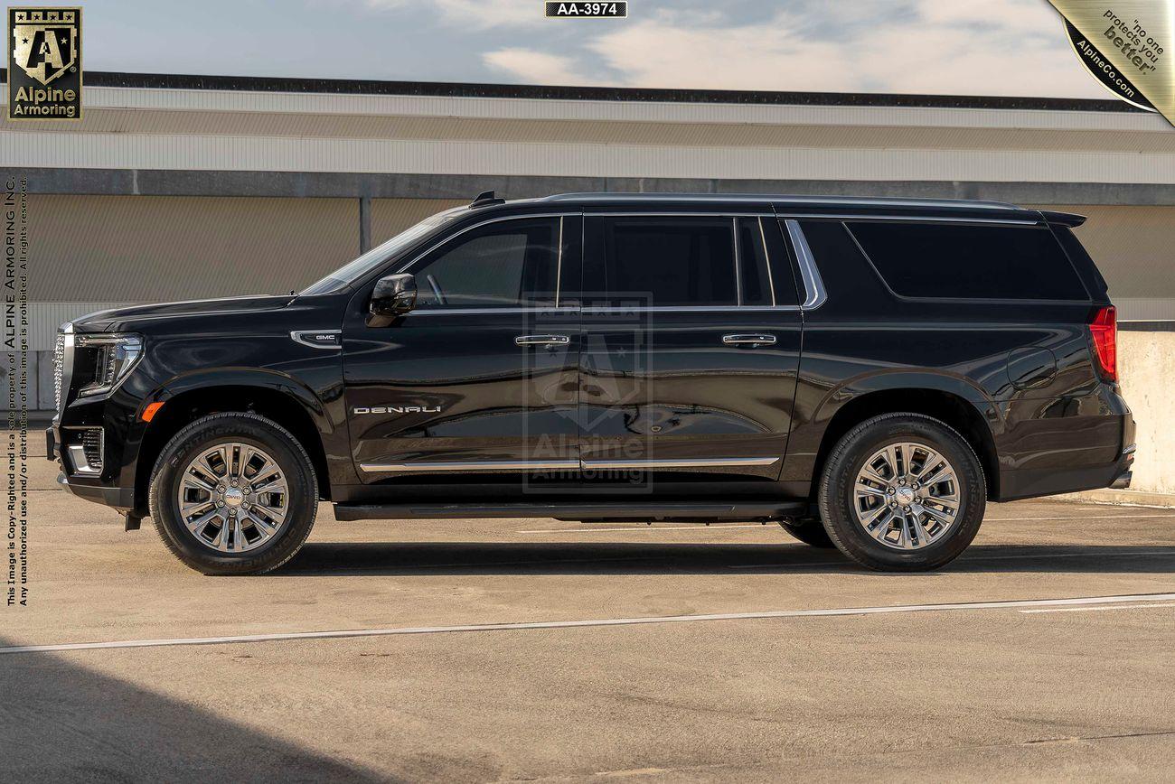 A black armored GMC Yukon Denali XL SUV is parked in an outdoor area in front of a building. The vehicle appears clean and polished with shiny detailing.