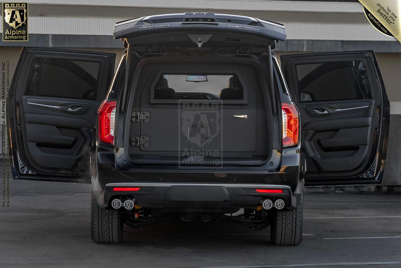 A black armored GMC Yukon Denali XL SUV with all doors open, revealing a customized and secure passenger cabin and trunk area with visible metal  barriers and partitions.