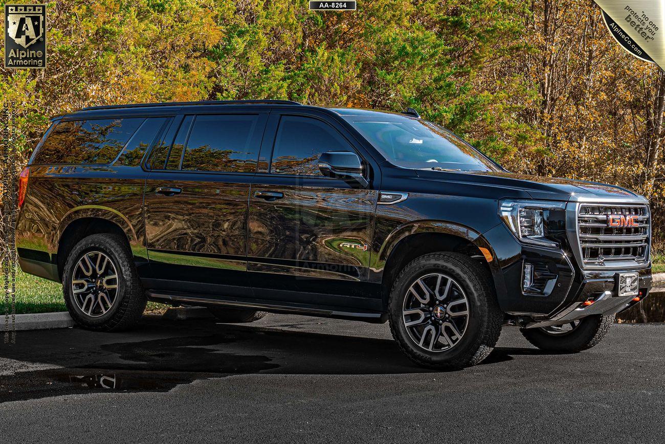 A black GMC Yukon XL AT4 SUV is parked on the pavement with a backdrop of green and brown foliage.