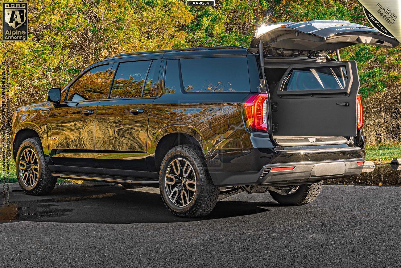 A black GMC Yukon XL AT4 SUV is parked on a paved surface with its rear hatch open, revealing additional storage space. The vehicle is surrounded by green foliage.