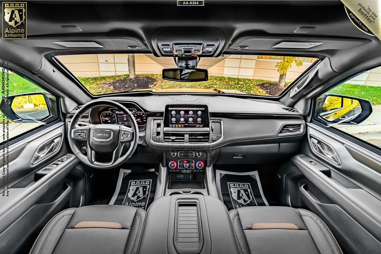 Interior of an armored GMC Yukon XL AT4 showcasing the dashboard, steering wheel, touchscreen display, and front seats with Alpine Detailing floor mats.