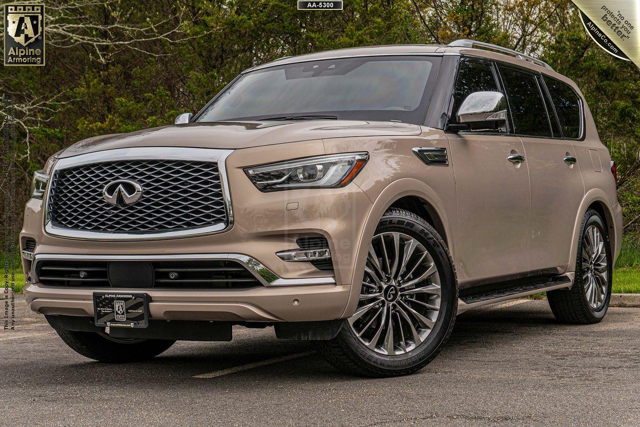 A beige INFINITI QX80 SUV is parked outdoors on a paved surface with some greenery in the background. The vehicle features a prominent front grille and chrome accents.