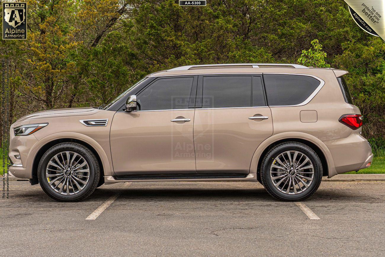 Driver side view of a beige INFINITI QX80 SUV parked on a road with green trees in the background.