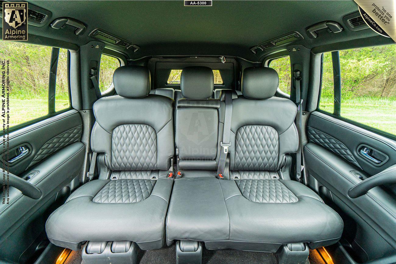 Interior view of a INFINITI QX80's back seats, featuring three gray quilted leather seats with headrests and a green landscape visible through the windows.