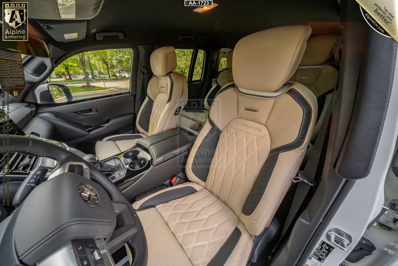 Interior view of an Armored Toyota Land Cruiser 300  showcasing beige leather seats and detailed stitching, with a clear view of the driver and passenger seats, the steering wheel, and the center console.