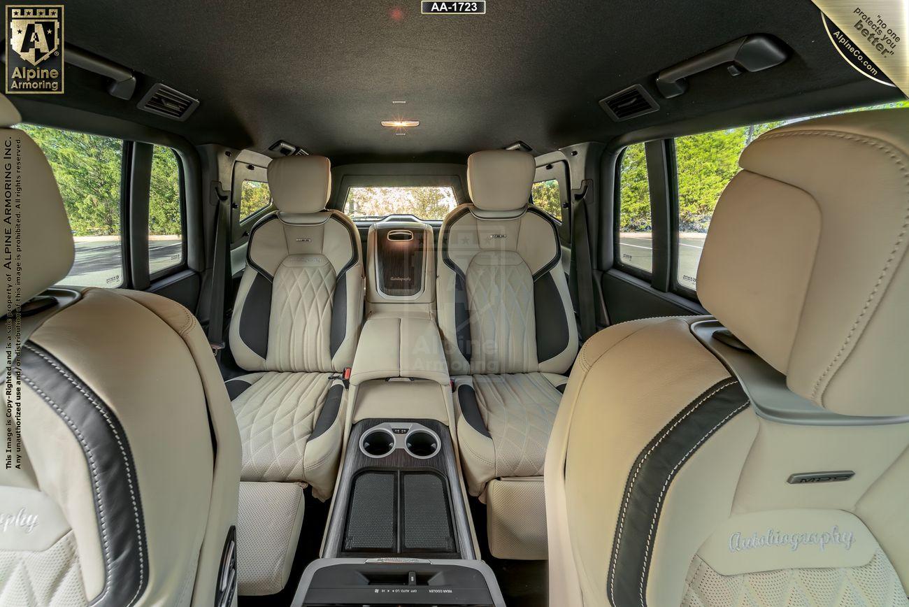 Interior view of an Armored Toyota Land Cruiser 300  showcasing beige leather seats, dual cup holders, and a center console, with scenic greenery visible through the windows.