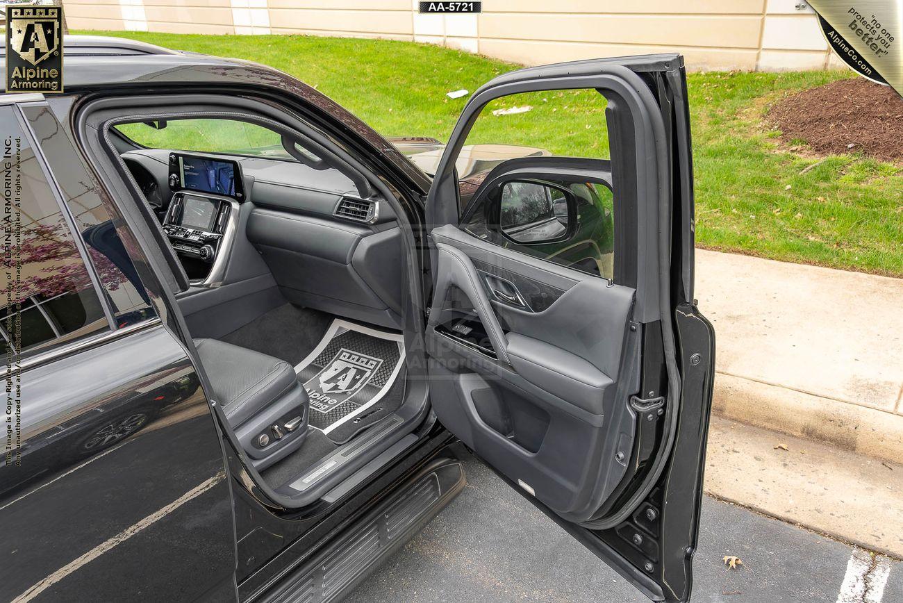 Interior view of an armroed Lexus LX600 Luxury sedan with leather seats and a modern dashboard featuring a large central touchscreen display and various controls. The steering wheel prominently displays the Lexus logo.