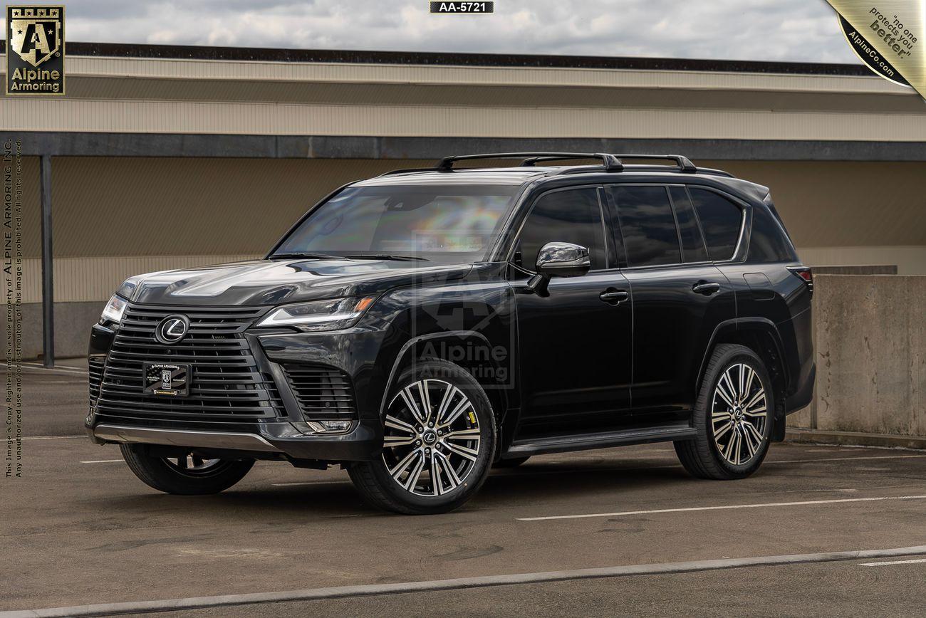 A black armroed Lexus LX600 Luxury SUV is parked in an outdoor setting next to a concrete barrier with a building in the background.