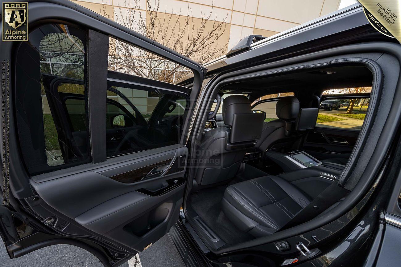 A black armored Lexus LX600 Ultra Luxury with all doors open showcasing a spacious interior with black seats and modern dashboard. The setting is an outdoor parking area near a building.