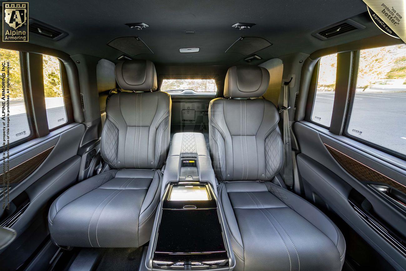 Interior of an armored Lexus LX600 Ultra Luxury featuring two large, grey leather seats with a central console, advanced control panel, and sleek wood trim accents. The view shows the back portion of the front cabin.