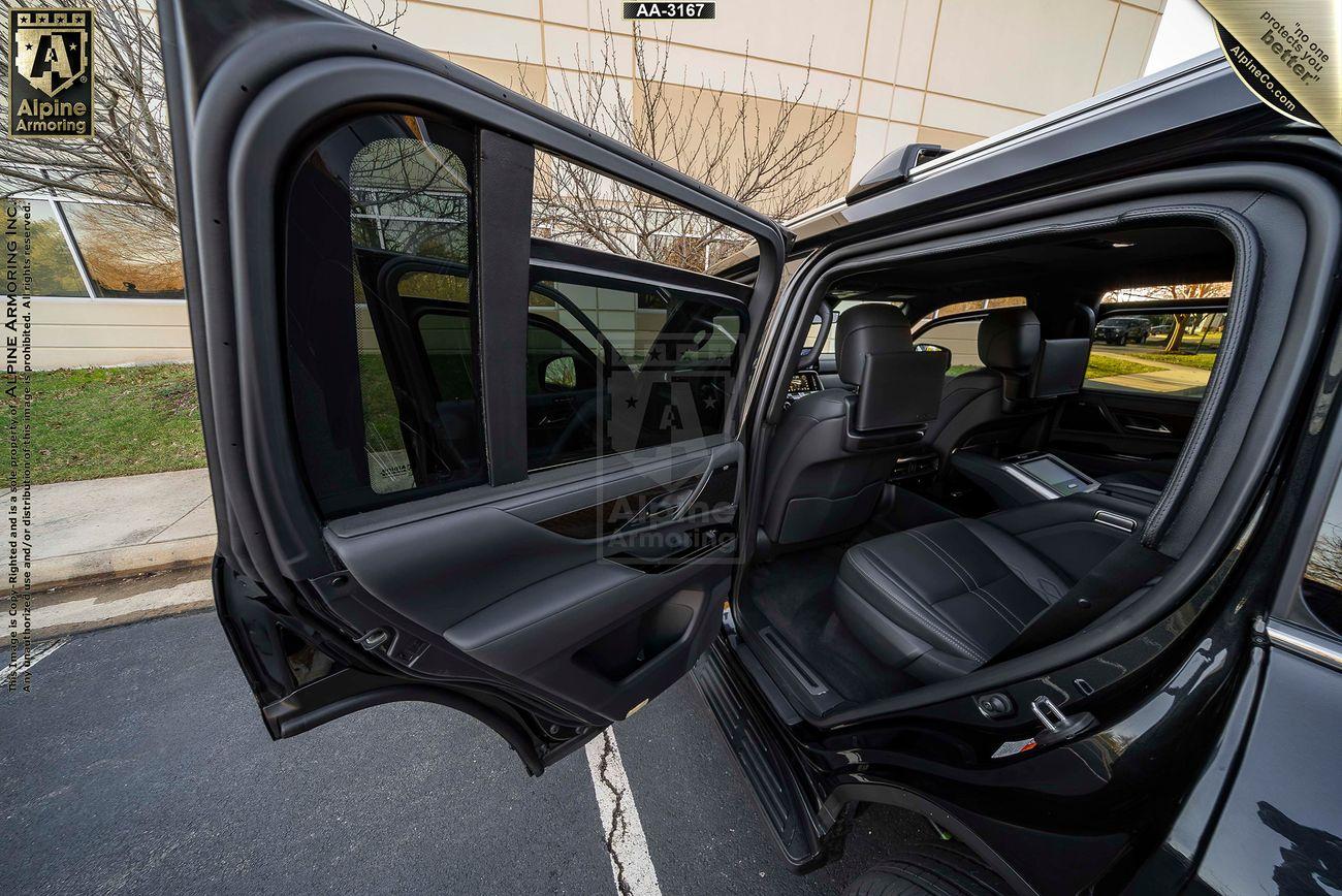 An open rear car door of a Lexus LX 600 Ultra Luxury reveals a black leather interior with spacious seating and a view of a building exterior through the windows.