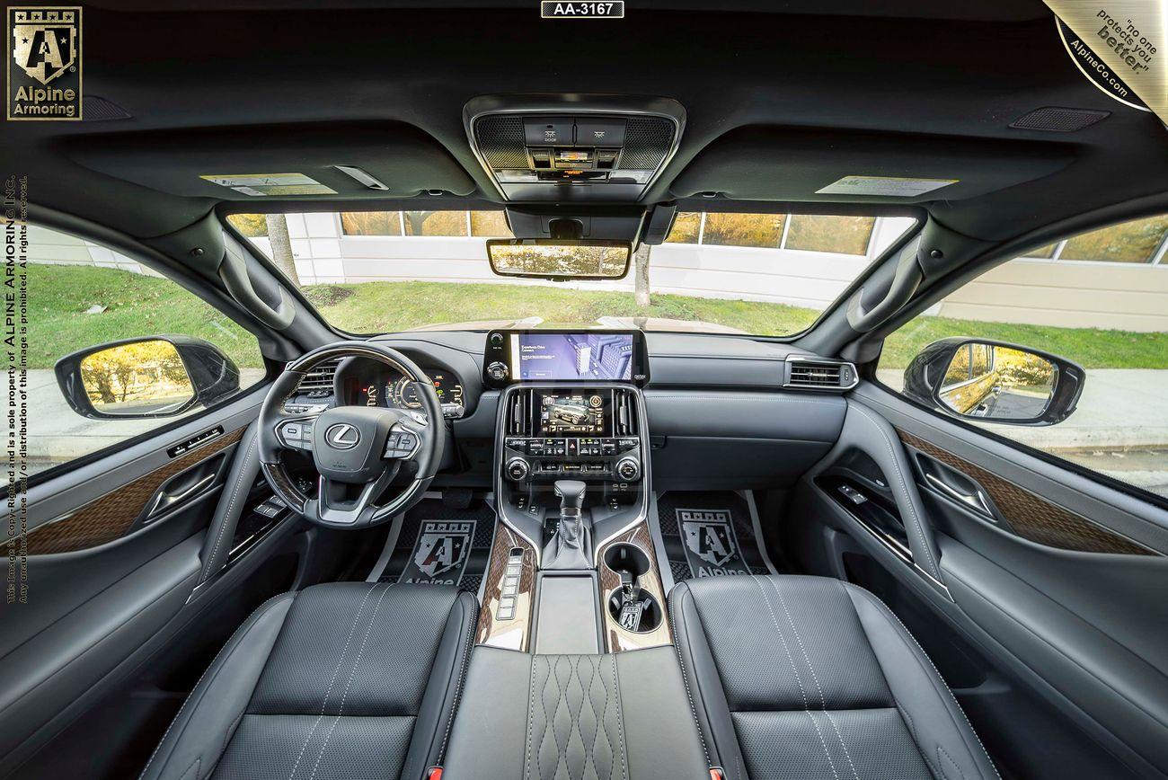 Interior view of a Lexus LX 600 Ultra Luxury SUV showcasing the dashboard, steering wheel, and infotainment system. Leather seats and detailed wood paneling are visible, along with a sunroof and exterior scenery.