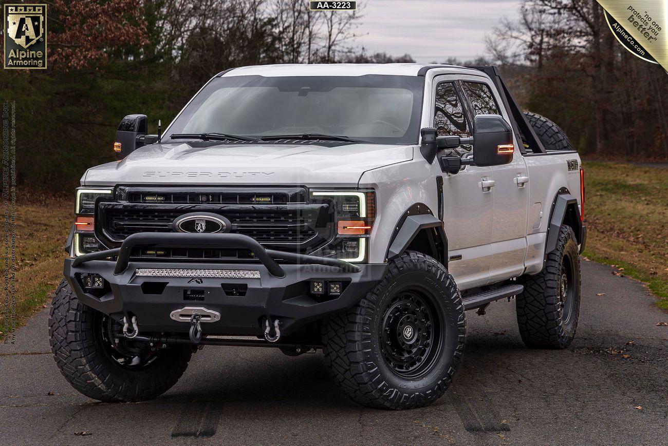 A white, off-road Mastiff truck equipped with large tires, custom front bumper, and additional accessories is parked on a road with trees in the background.