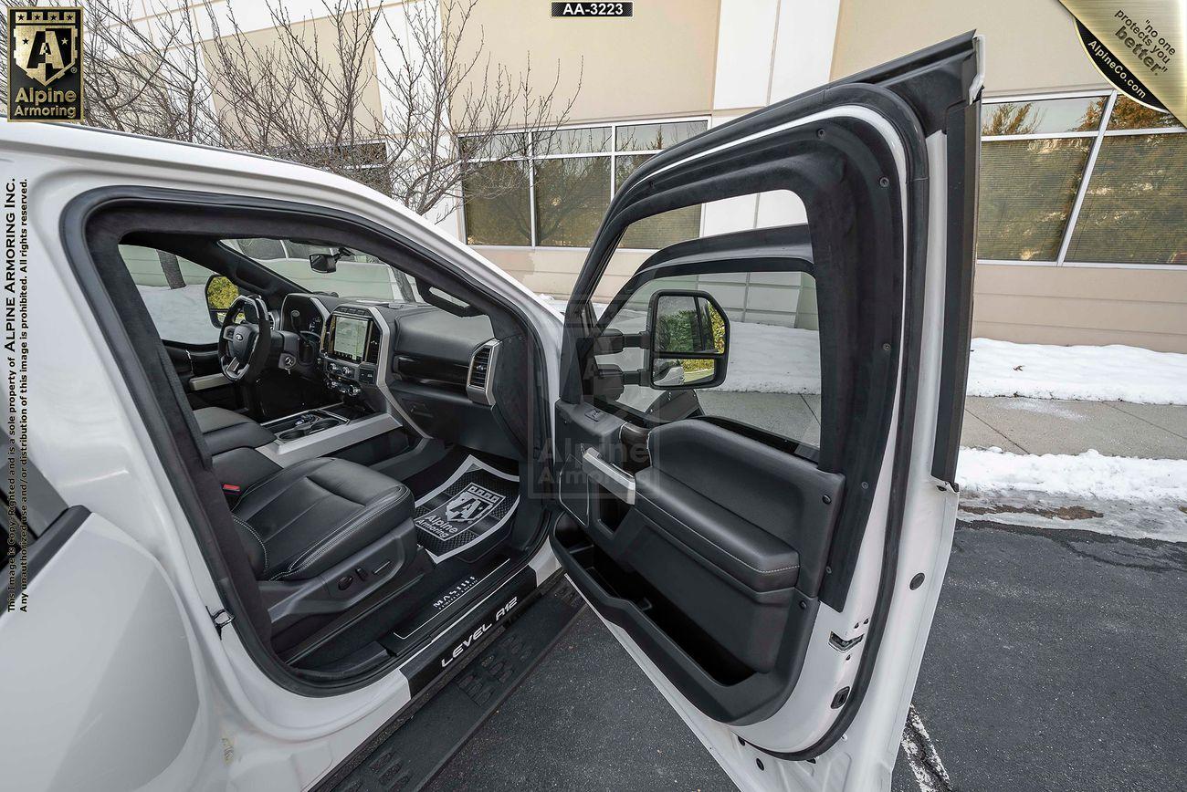 Passenger side view of the interior of a white Mastiff with both the driver and passenger doors open, showing black seats and dashboard. Snow is visible outside the vehicle, along with a building in the background.