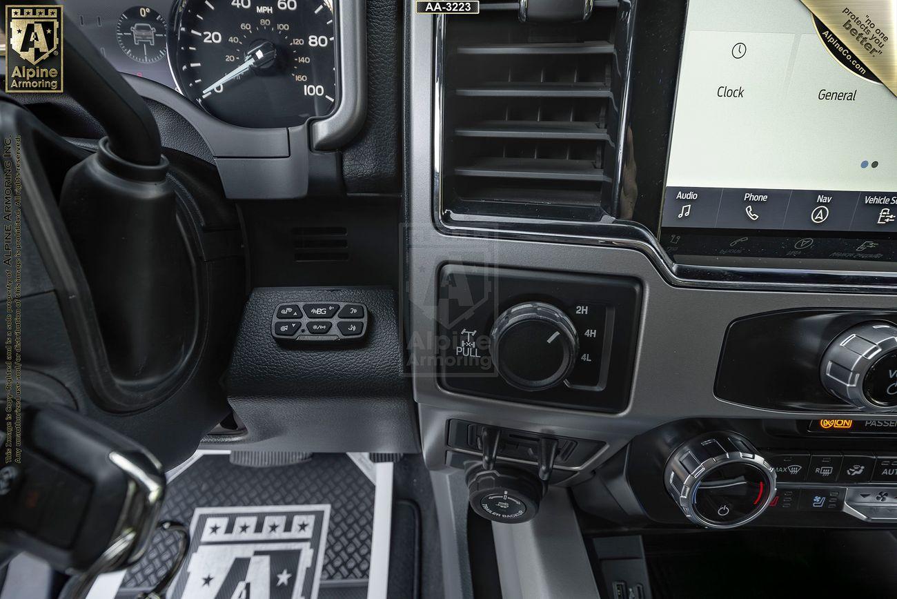 Close-up view of a Mastiff's dashboard, displaying various control buttons, a speedometer, and a touchscreen display showing clock and general settings. The Alpine Armoring logo is visible on the mat and screen.