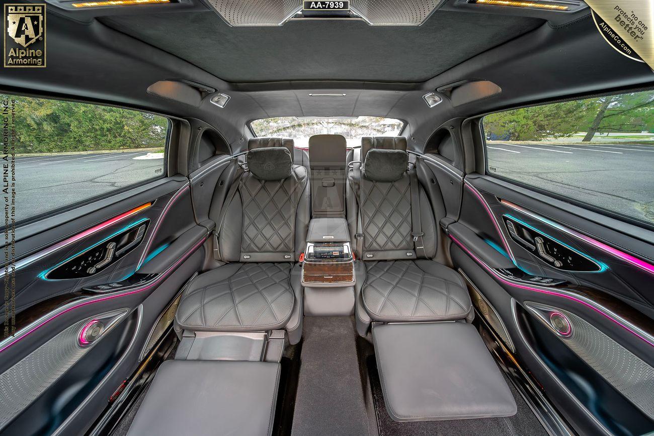 Mercedes-Benz Maybach interior featuring quilted leather seats, ambient lighting, and a central control panel. The image shows the rear seating area of the vehicle with ample legroom and sophisticated design elements.