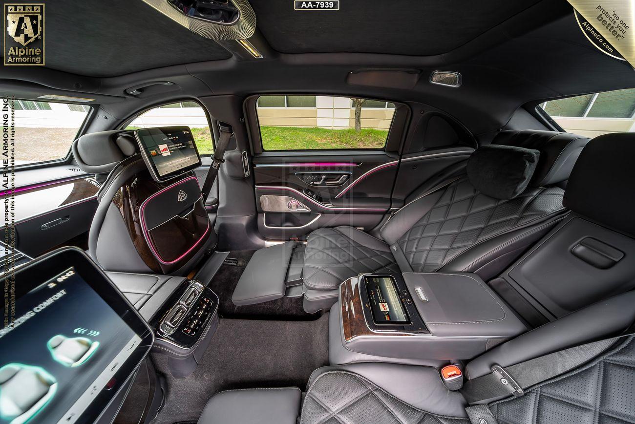 Interior of a luxurious Mercedes-Benz Maybach showcasing spacious black leather seats, high-tech control panels, and entertainment screens. The design features quilted stitching and modern amenities.