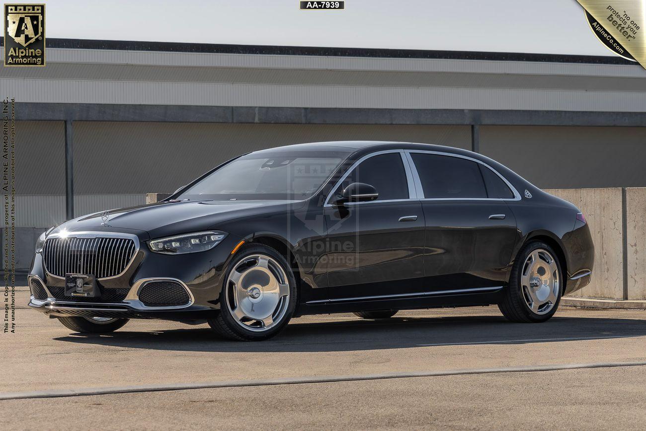 A black luxury Mercedes-Benz Maybach with chrome accents, parked in front of a building. The car features a sleek design, alloy wheels, and tinted windows. Logo indicates Alpine Armoring modifications.